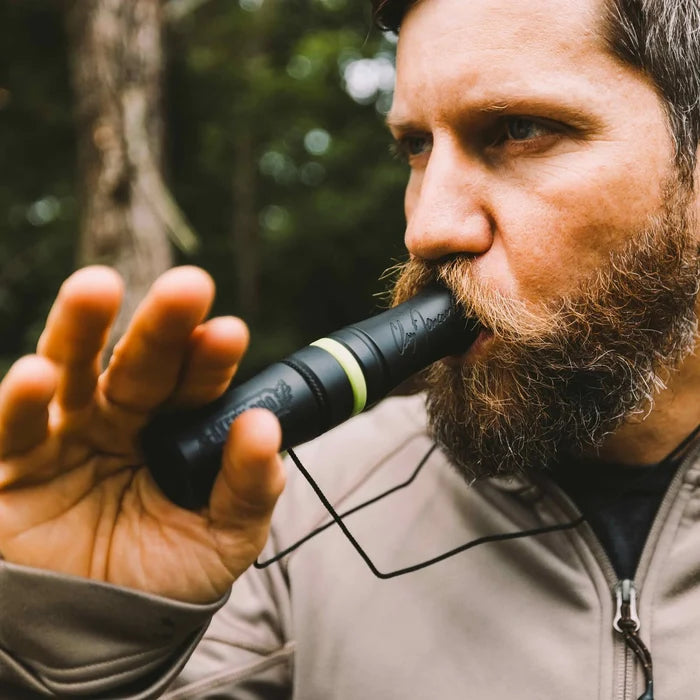 A bearded man blows a black Claw Blaster Pro game call with a bright green band, featuring a Clay Dawson signature and attached black lanyard.