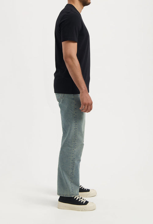 Sustainable MUD Jeans in dark blue denim, styled with a matching jacket and white sneakers, emphasizing ethical fashion.