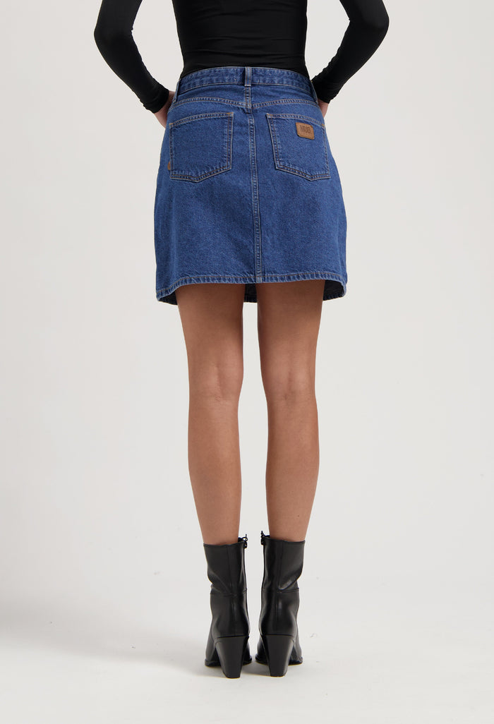Denim A-line skirt in blue from MUD Jeans, paired with black leather ankle boots and a fitted long-sleeve black top.