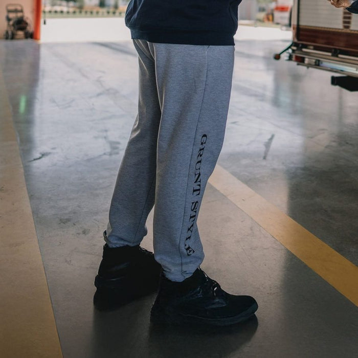 Person wearing gray sweatpants with 'Grunt Style' text and black shoes in an indoor setting.