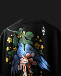 A black crewneck t-shirt featuring a large graphic print of two blue birds, green leaves, yellow flowers, and a pinkish-orange flower on the front. A small white logo is printed on the upper right shoulder area.
