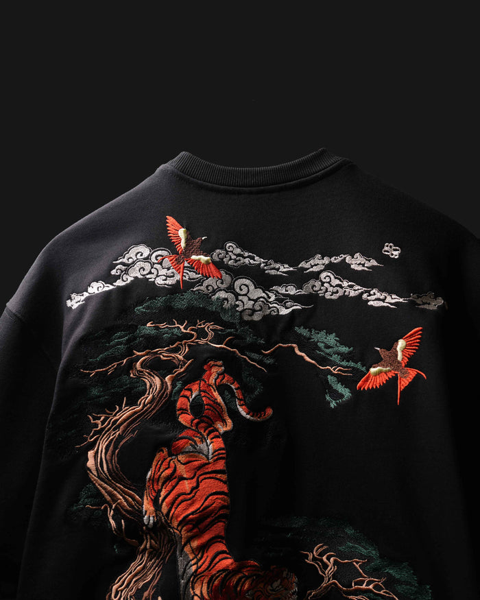 Close-up of a black crewneck sweatshirt featuring a large Japanese-style graphic print of a tiger, clouds, and red birds on the front.