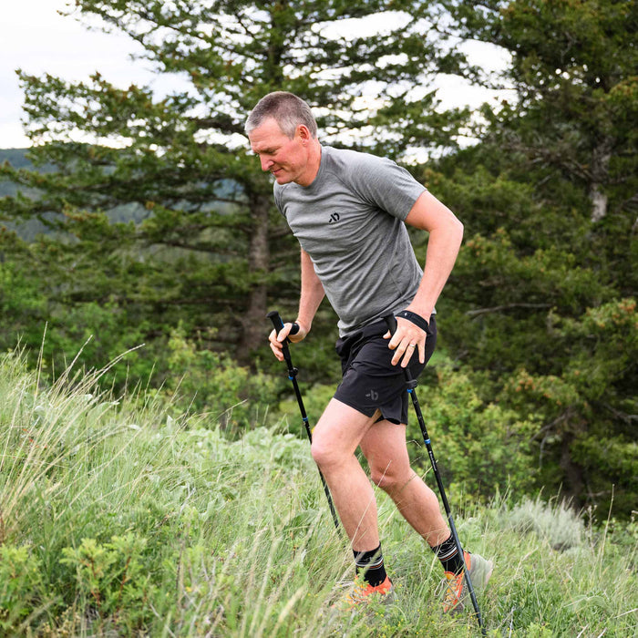 Man trail running with trekking poles in a forested area