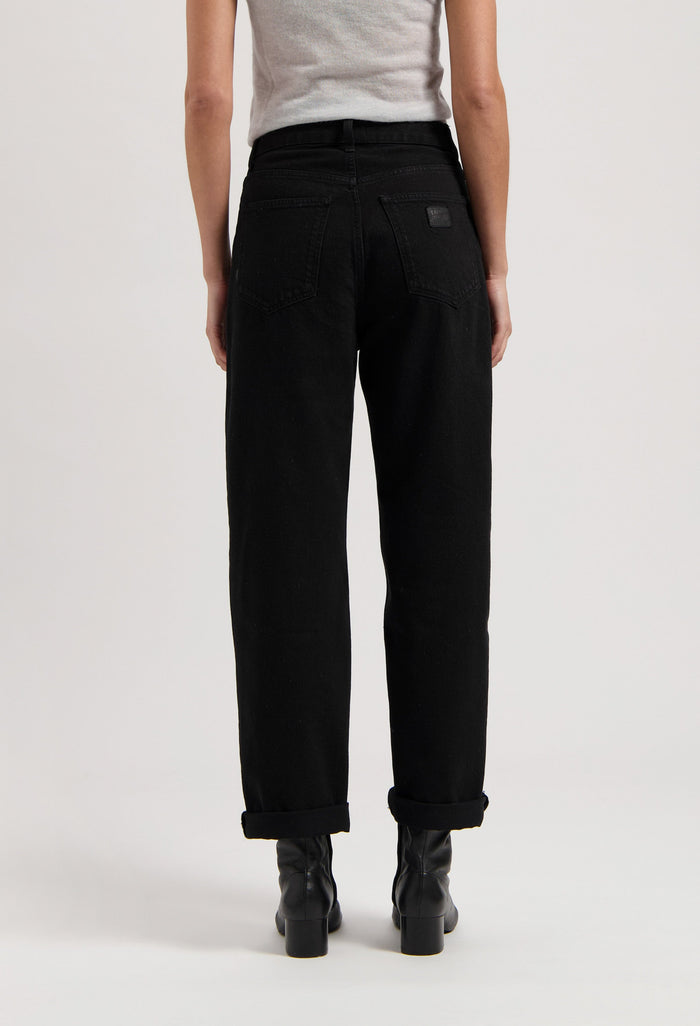 Black high-waisted jeans made of cotton, shown from the back, paired with black boots and a light gray sleeveless top.