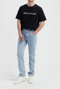 Sustainable MUD Jeans in light blue denim, featuring a classic fit, ethically made, worn with a white tee and sneakers.