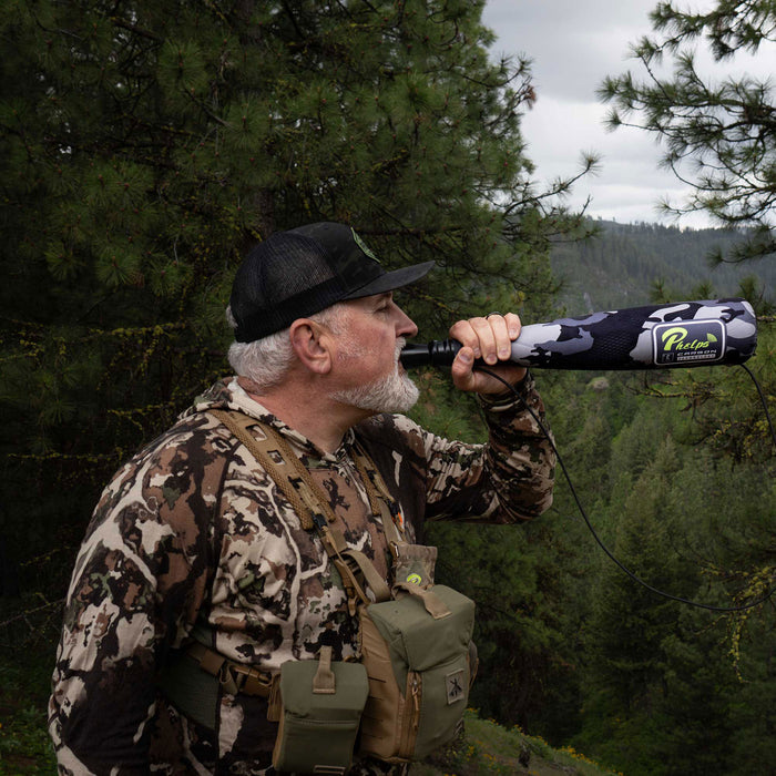 Man holding a grey and black camouflage Phelps elk call with a visible logo to his mouth.
