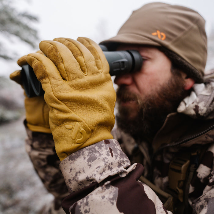 Tan leather gloves featuring an embossed logo, worn by a person looking through binoculars.