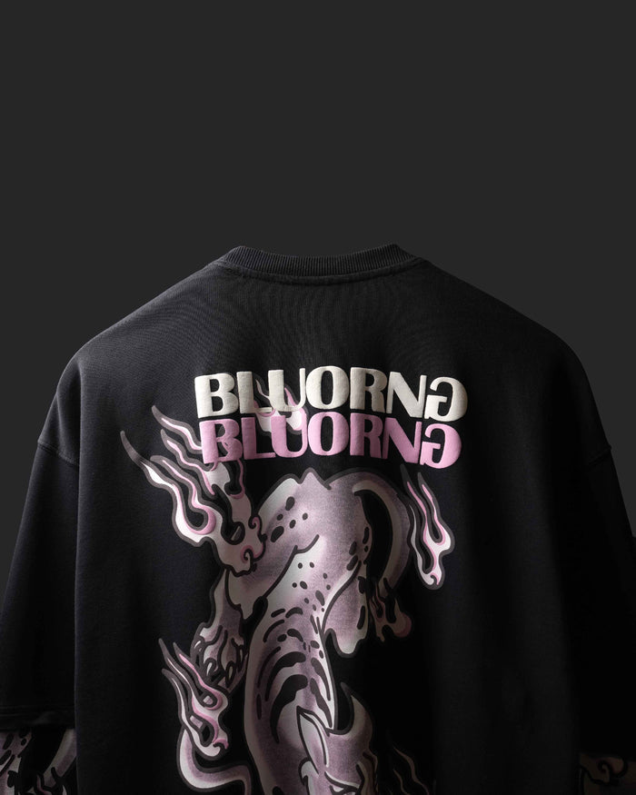 A black oversized t-shirt featuring a large graphic print on the back. The design includes the word 'BLUORNG' in white and pink lettering above a stylized, metallic pink and silver creature with flame-like details, set against a dark background.
