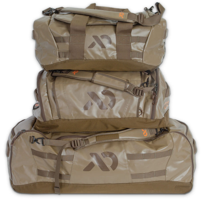 Three stacked coyote brown First Lite duffel bags with prominent FL logos, top handles, and zippered side pockets.