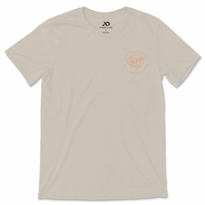 Light tan t-shirt with a pale orange circular graphic on the left chest featuring an eagle and text, plus a First Lite neck label.