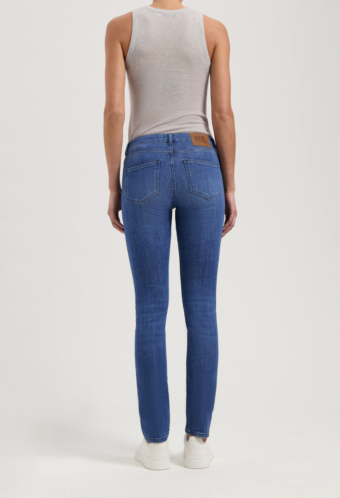 Back view of person wearing straight-fit MUD Jeans in classic blue denim, with a sleeveless gray top and white sneakers.