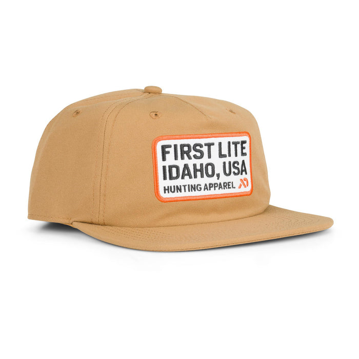 Tan cap with a white embroidered patch featuring "FIRST LITE IDAHO, USA HUNTING APPAREL" in black text with an orange border.