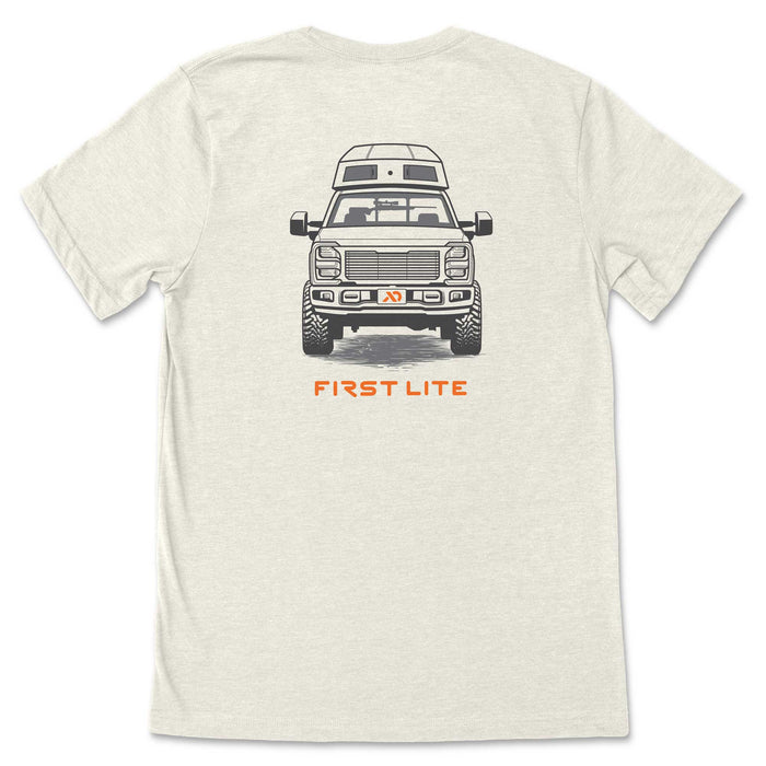 Heather cream t-shirt with a graphic of a front-facing pickup truck, a camper top, off-road tires, a rifle visible through the windshield, and orange "FIRST LITE" text.