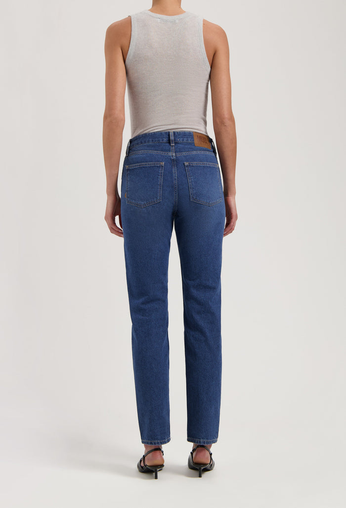 Person wearing sustainable dark blue denim jeans with a white sleeveless top, showcasing the back view and fit.