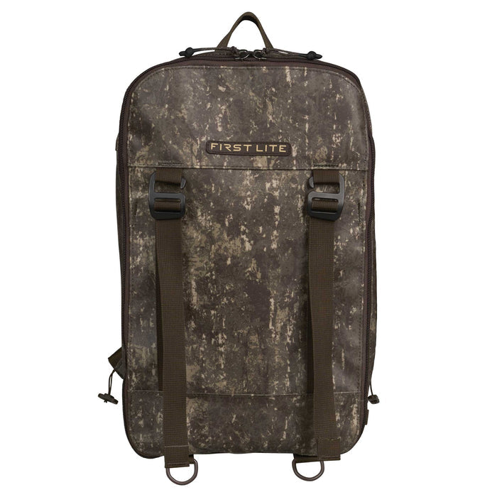 First Lite camouflage pack featuring a top handle, two front webbing straps with buckles, and two bottom D-rings.