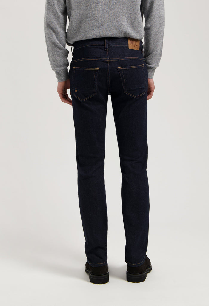 Sustainable MUD Jeans in dark denim, featuring ethical craftsmanship and classic stitch detail, paired with a gray sweater.