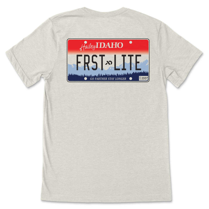 A heather grey t-shirt features a red, white, and blue license plate graphic with "Hailey IDAHO", "FRST-LITE" over mountains, and "GO FARTHER STAY LONGER EST 2007".