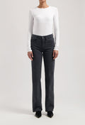 Model wearing high-waisted, black denim jeans paired with a white long-sleeve fitted top and black pointed shoes.