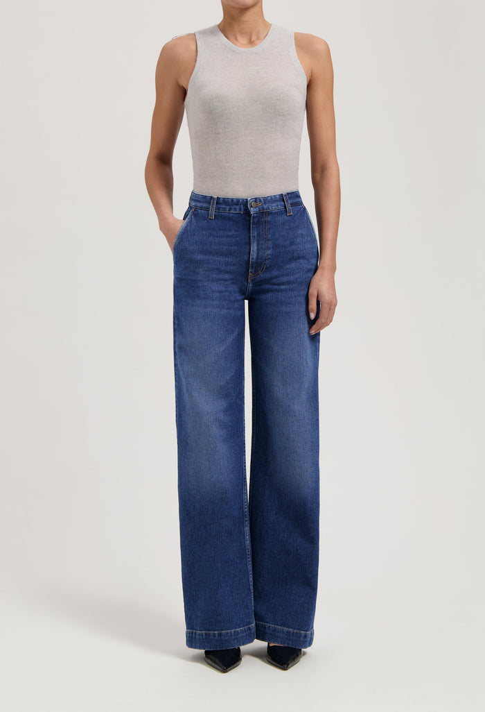 Woman wearing wide-leg blue denim jeans paired with a sleeveless light gray top in a minimalist style.