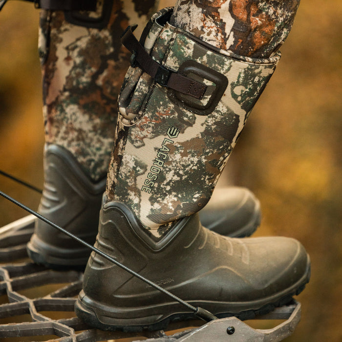 Dark green and camouflage LaCrosse hunting boots with an upper strap, standing on a metal grate.
