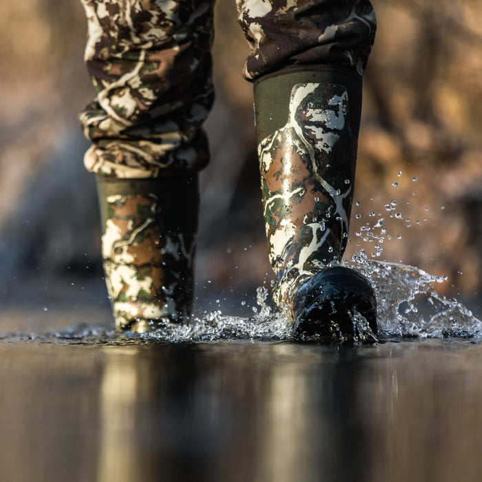 Tall LaCrosse camouflage rubber boots with matching pants splash in water.