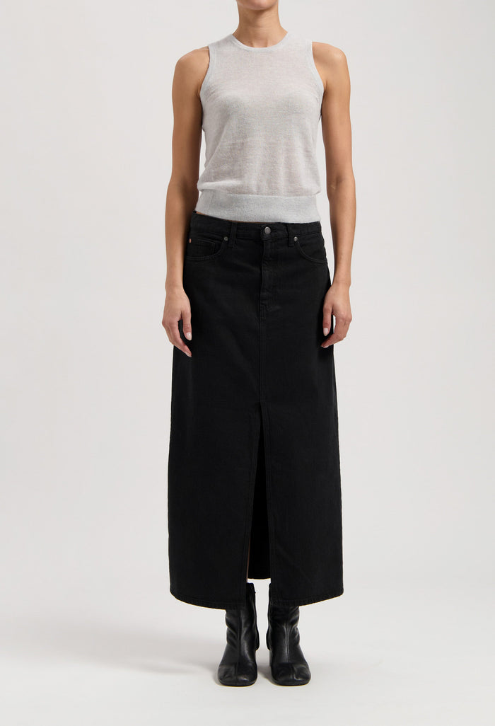 Model wearing a sleeveless gray top with a long black denim skirt, featuring a central slit, and black ankle boots.