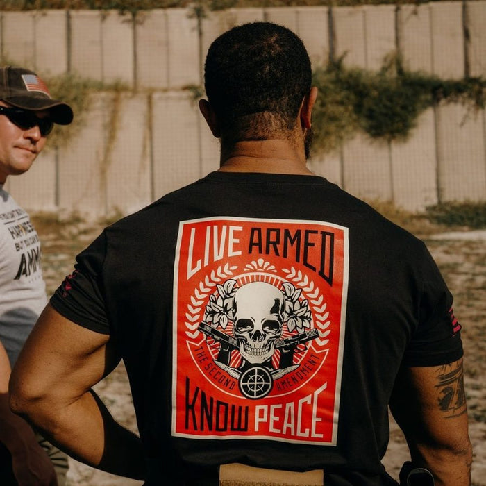 Person wearing a black t-shirt with a graphic design and text, standing outdoors.
