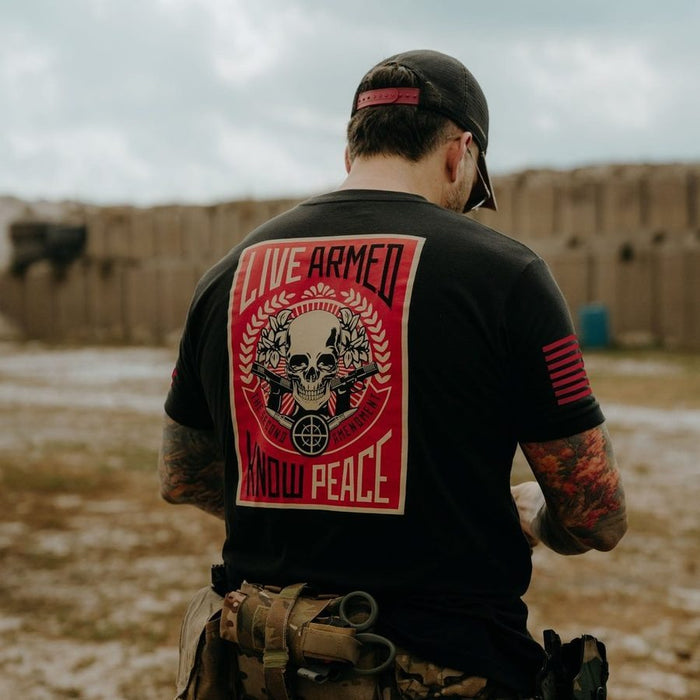 Person wearing a black t-shirt with a red and white graphic design, standing in an outdoor setting.