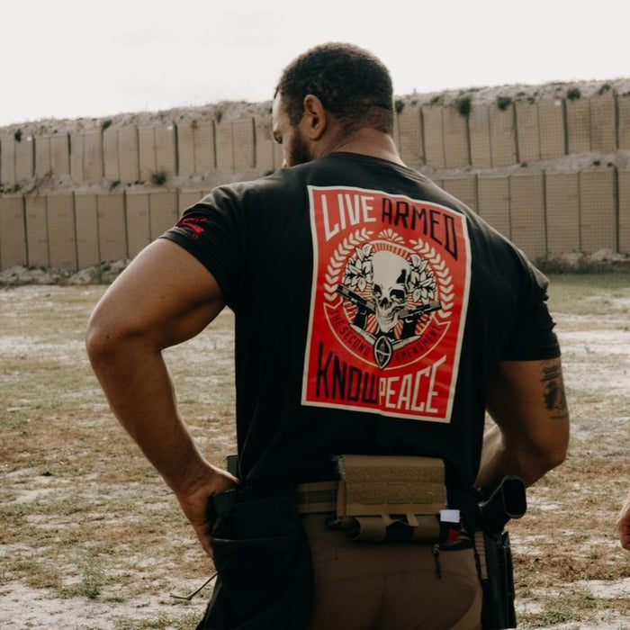 Person wearing a black t-shirt with a graphic design and text, standing in an outdoor setting.