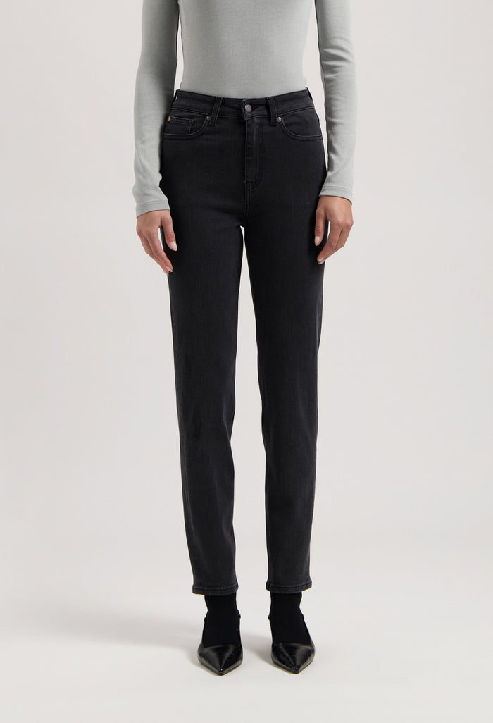 Person wearing black straight-leg jeans with a high-waist fit, paired with a light gray long-sleeve shirt and black heels.