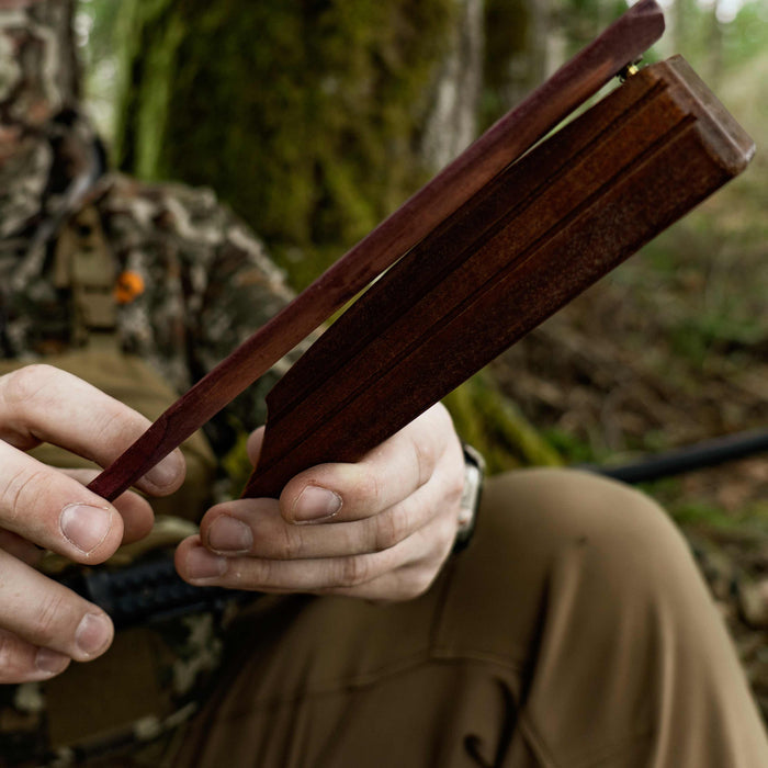 Dark reddish-brown wooden box call with a hinged paddle and brass pivot, held in hands.