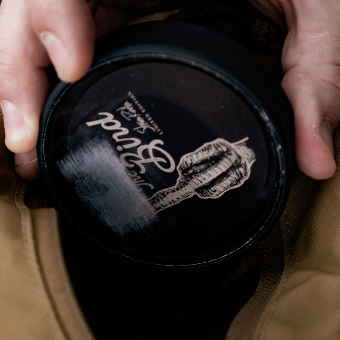 A person's hands hold a round black The Bind Limited Edition tin featuring a logo of a hand holding a quill on its lid.