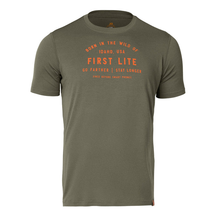 An olive green t-shirt features orange text on the front saying 'Born in the Wild of Idaho, USA First Lite Go Farther | Stay Longer Since Before Smart Phones' and a small brown tag on the lower right hem.
