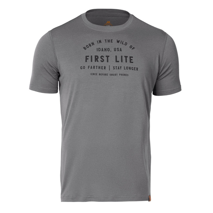 A grey t-shirt with "BORN IN THE WILD OF IDAHO, USA FIRST LITE GO FARTHER | STAY LONGER SINCE BEFORE SMART PHONES" printed on the chest and a small brown tag on the bottom right hem.