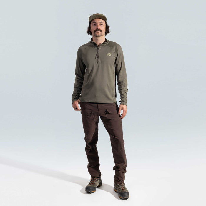 Man wearing a green quarter zip and brown pants on a light gray background