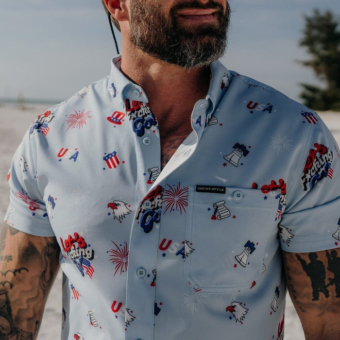 Man wearing a light blue button-up shirt with patriotic designs on a beach.
