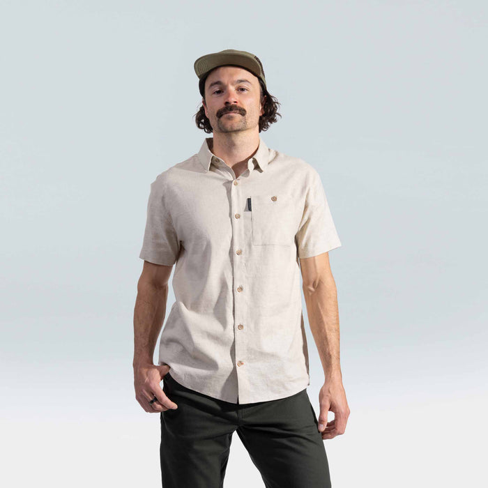 Man wearing a beige short-sleeve shirt and cap against a light gray background