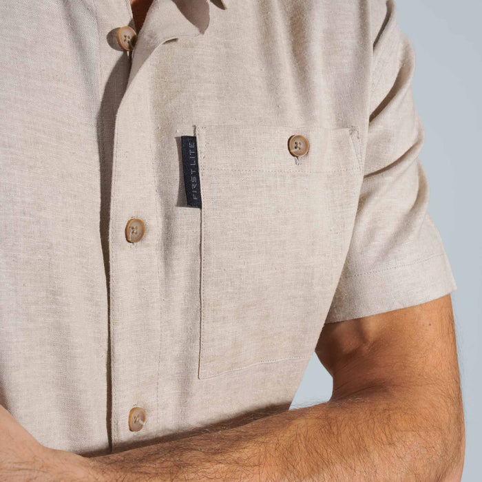 Close-up of a beige shirt with a First Lite label on a clear blue background