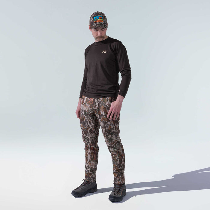 Man models a dark brown long-sleeve shirt with thumbholes, multi-tonal camouflage pants, and a matching camo hat with a colorful Bear Grease patch.