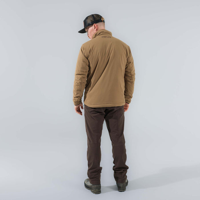 Man models a tan First Lite insulated jacket, dark brown pants, and a black mesh cap from behind.