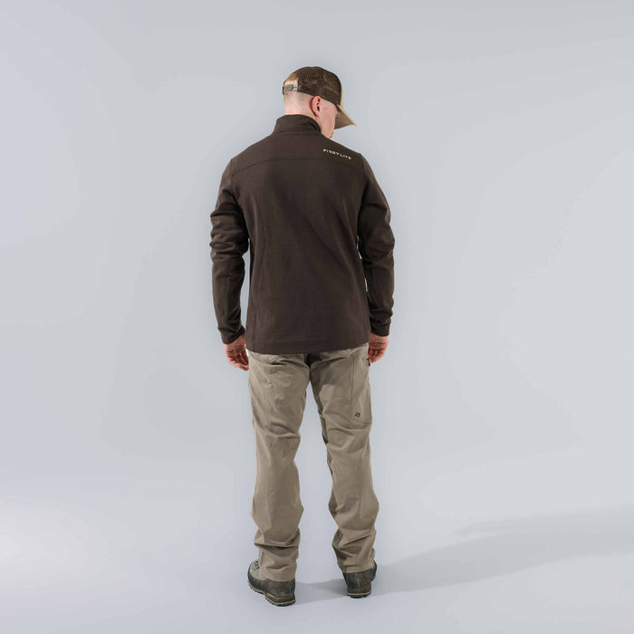 Rear view of a man wearing a dark brown quarter-zip fleece with the 'FIRST LITE' logo on the upper back, tan pants, and a camouflage hat.