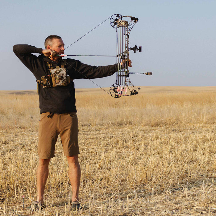 Dark camouflage compound bow with a multi-cam design and attached quiver, being aimed by an archer.