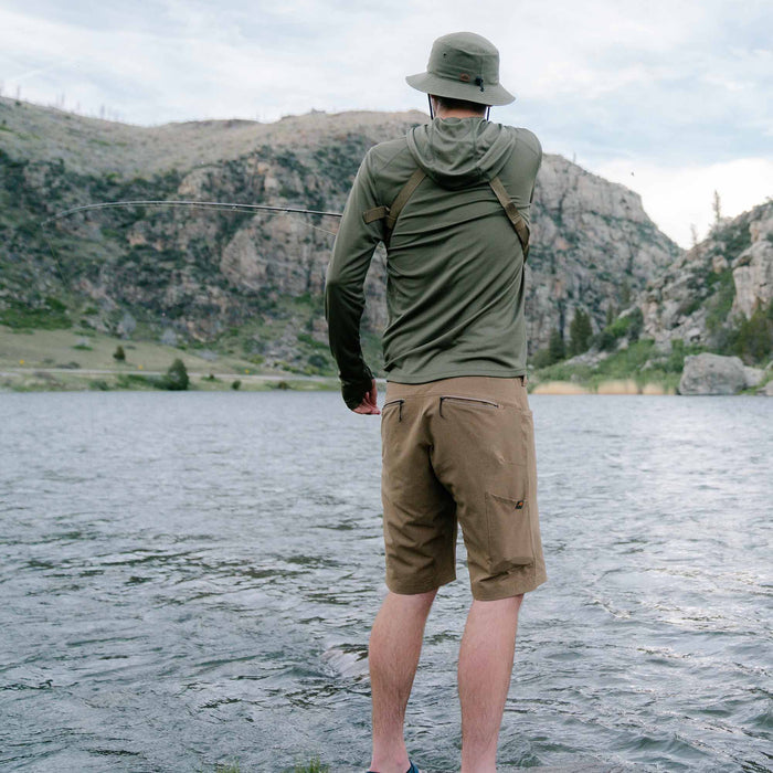 An olive green hooded long-sleeve shirt and matching boonie hat, with tan multi-pocket shorts, worn by a man fishing in a lake.