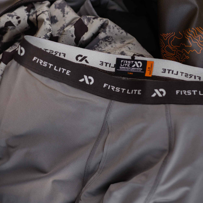 Grey men's First Lite Yuma base layer bottoms with a dark brown elastic waistband featuring the brand name.