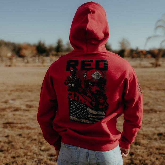 Person wearing a red hoodie with a graphic design and 'RED' text, standing in an open field.