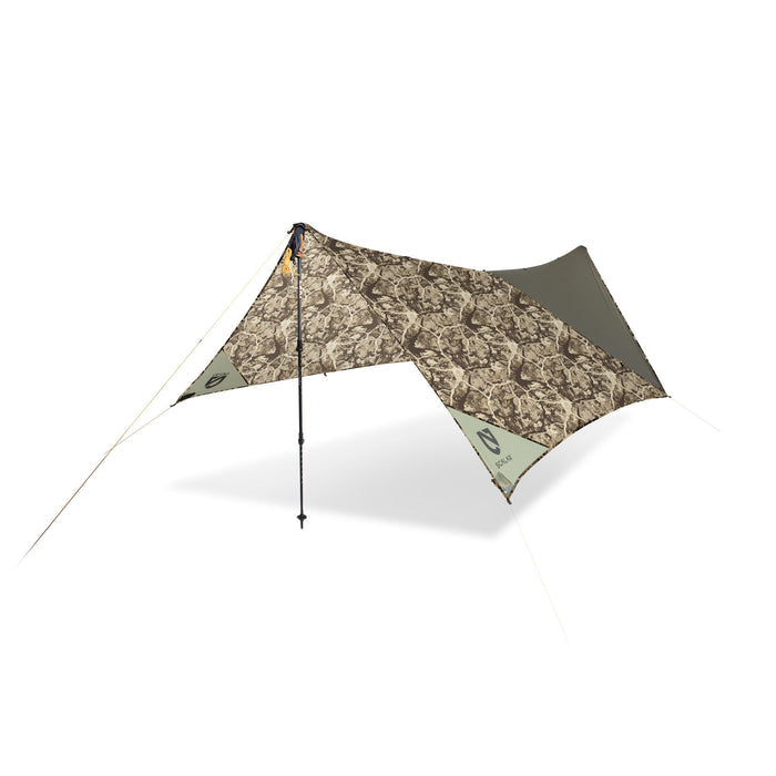 A camouflage and olive green camping tarp shelter is erected with a single trekking pole, showing guide lines and Nemo Scalar branding.