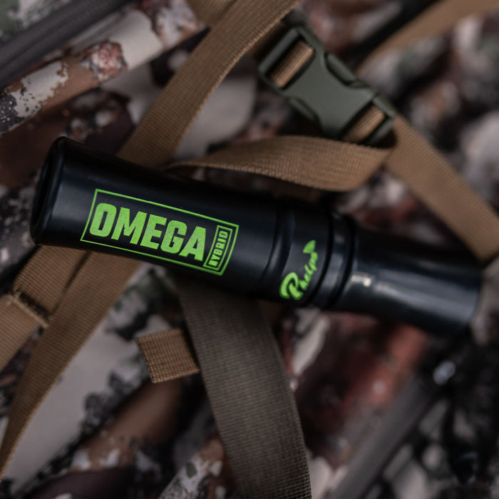 Black game call with green OMEGA HYBRID and Phelps branding, resting on a camouflage backpack.