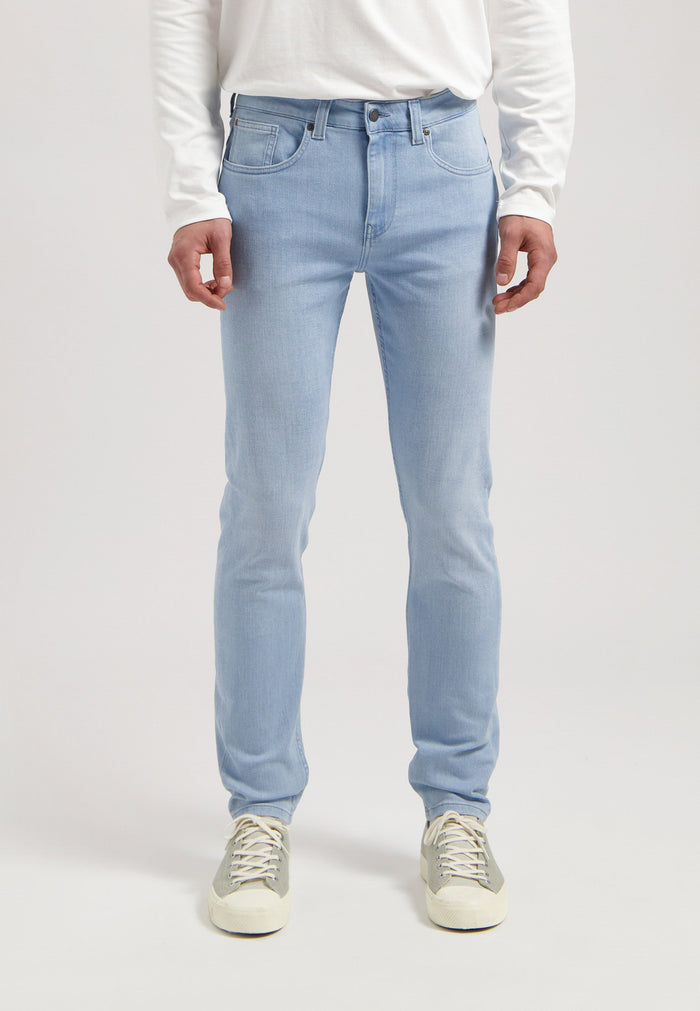 Sustainable MUD Jeans in dark denim, featuring a classic straight fit, paired with a light gray sweater and black boots.