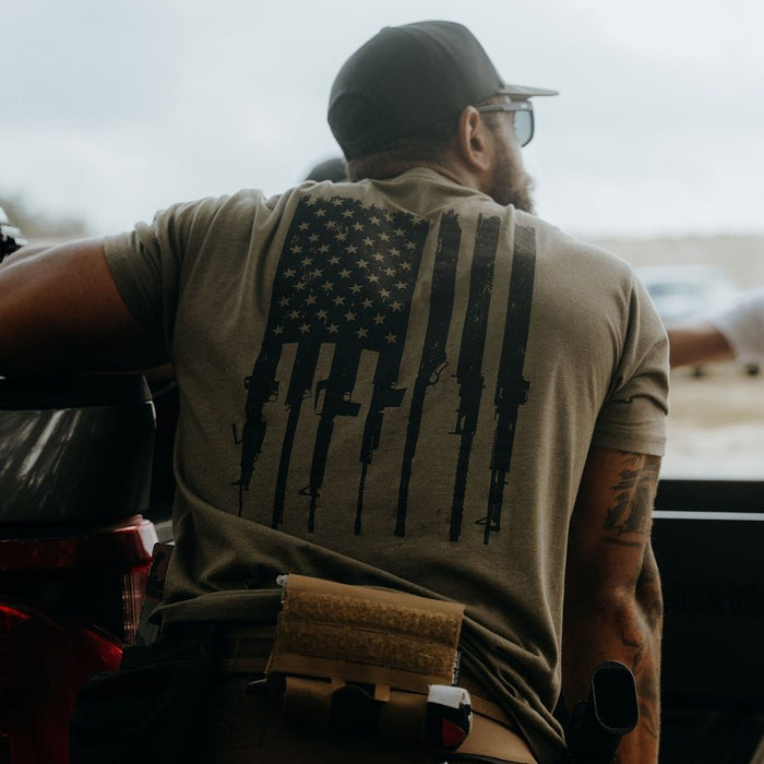 Man wearing a t-shirt with an American flag design, sitting on a bench.