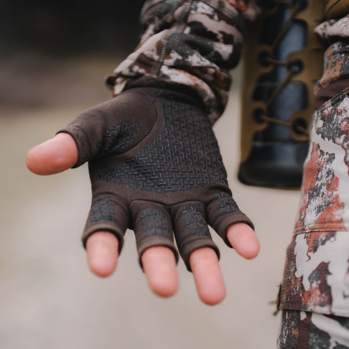 Close-up of a hand wearing a brown fingerless glove with a black textured grip pattern on the palm and a camouflage sleeve.